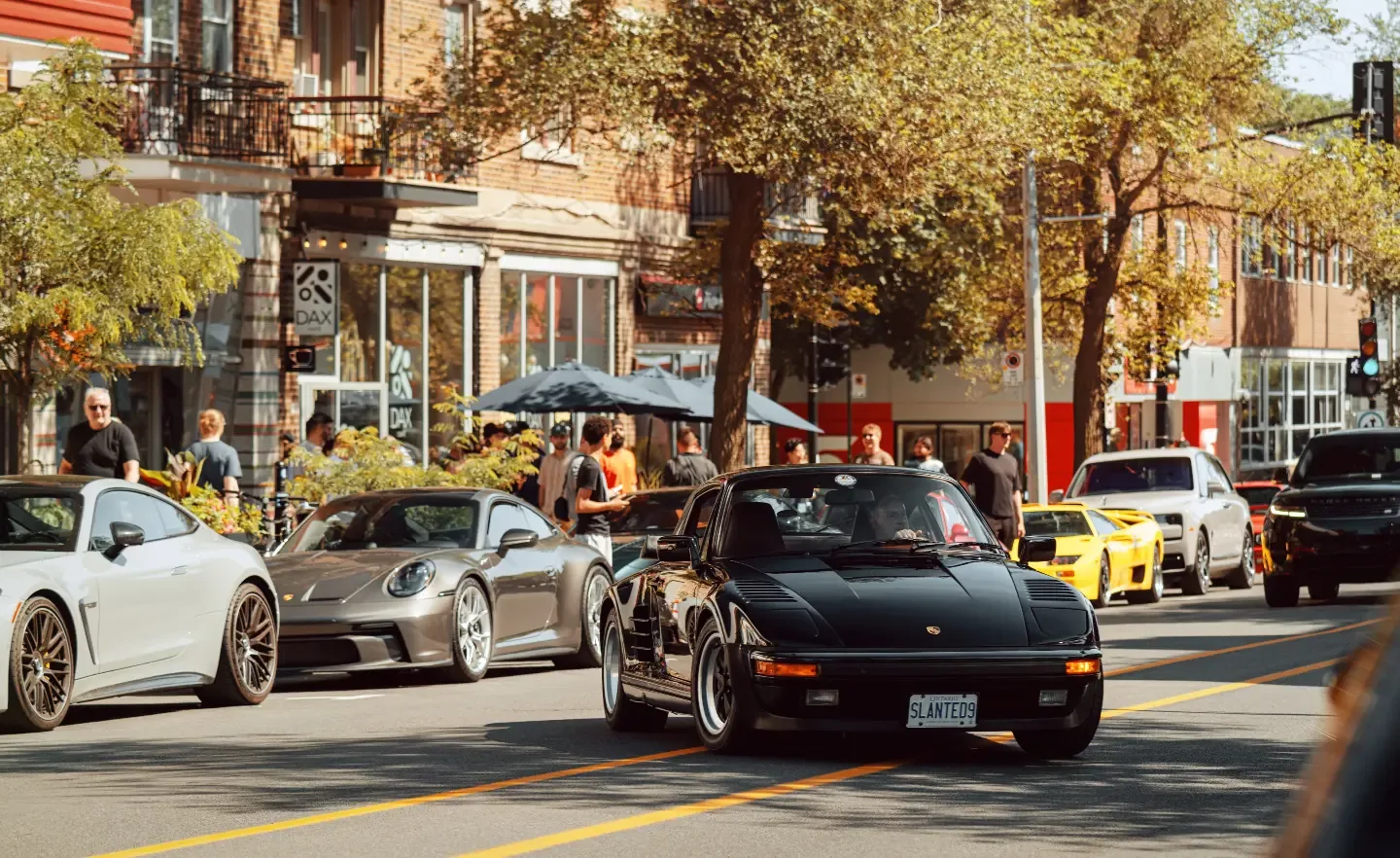 The line along the curb: a silver Mercedes, a black Porsche 911 and a yellow Lamborghini Diablo, with the crowd spilling onto the sidewalk.