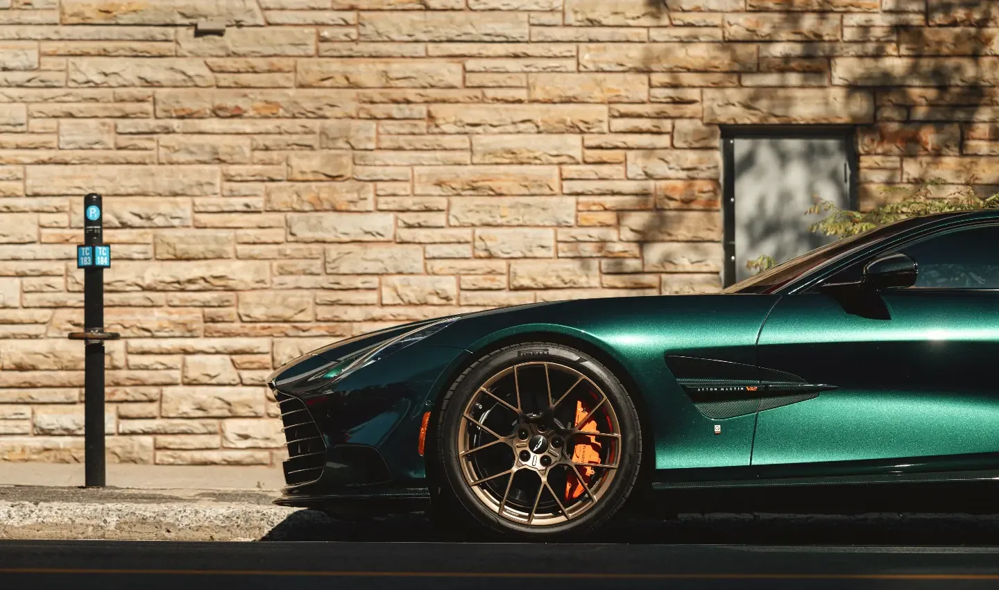 A green Aston Martin against a limestone wall, bronze wheels catching the light.