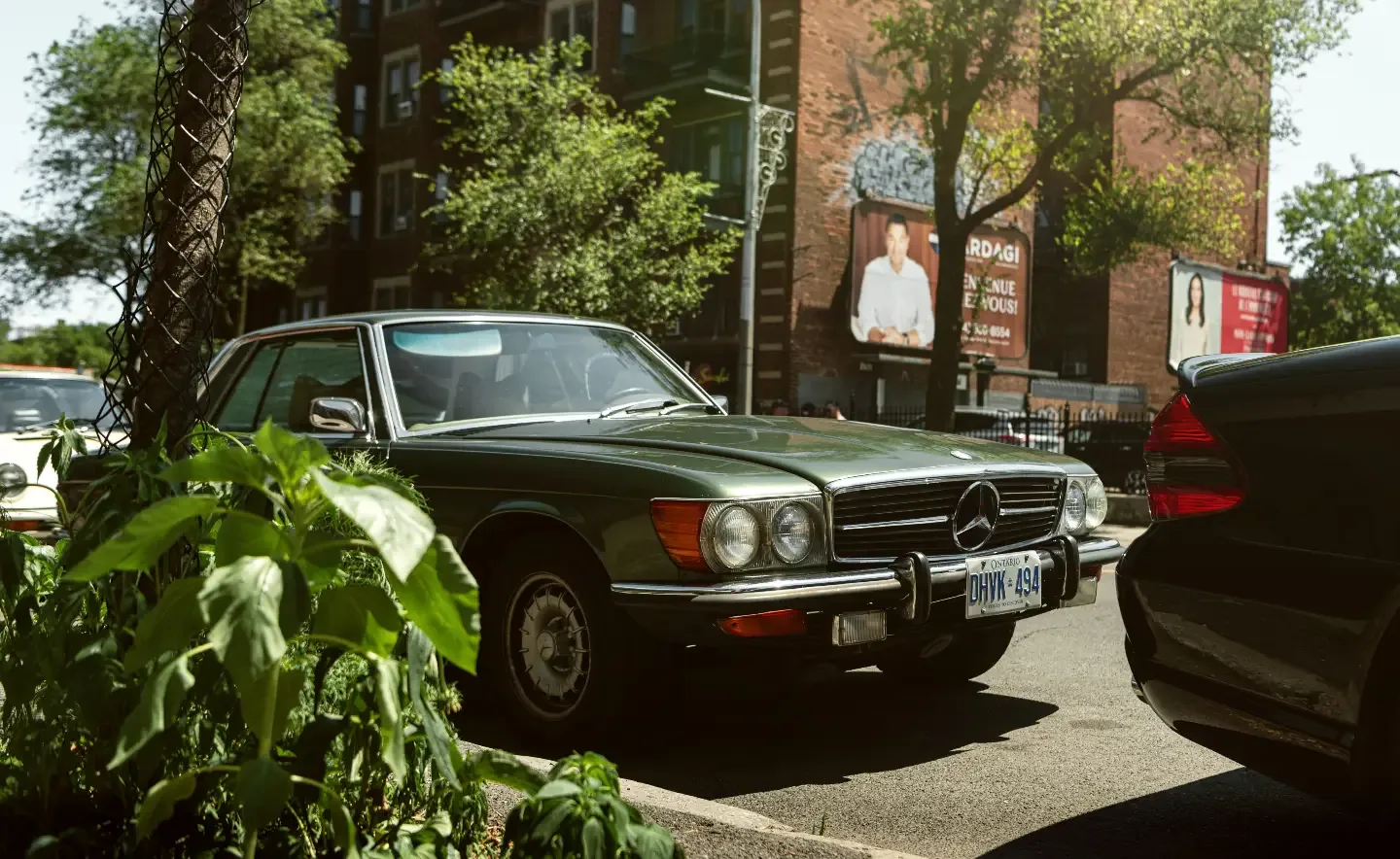A green Mercedes-Benz SL parked behind sidewalk planters.
